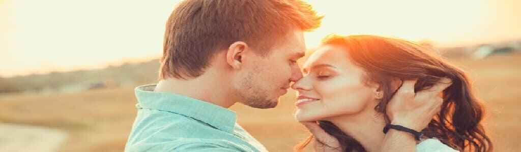 A man and woman stand nose to nose, smiling adoringly at each other as the golden hues of a brilliant sunset surround them. This intimate moment represents the Ways to Fire Up Your Relationship, offering Spiritual Solutions for Relationship healing and the Best Ways to Reignite Romance and Deepen Love.