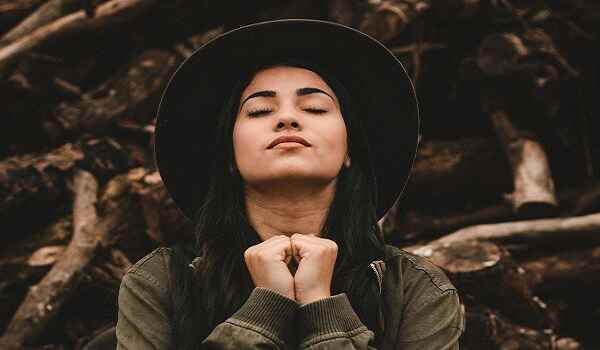 a young woman with eyes closed, head tilted upwards, hands together, is finding peace by praying Prayers for Anxiety Relief