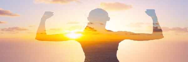 Woman facing sunset,
 arms raised in victory