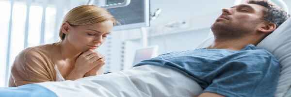 Man in hospital bed, wife praying healing prayers