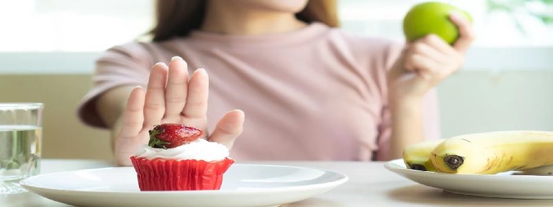 A determined woman sitting at a table, holding an apple in one hand while pushing a tempting cupcake away, symbolizing the power of self-discipline and resisting distractions to achieve personal growth.